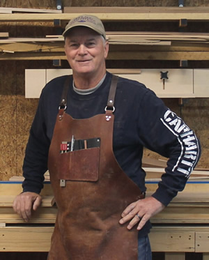 Dan Wallace standing in front of shelves of wood in his workshop.